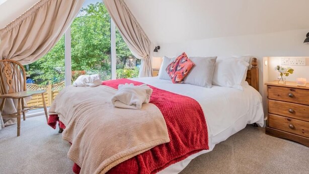 Een slaapkamer met een groot bed, een houten dressoir, een stoel en uitzicht op groen buiten.