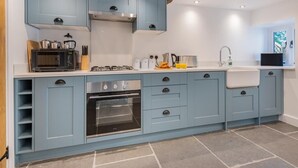 Een keuken met blauwe kastjes, een magnetron, een fornuis en een spoelbak.