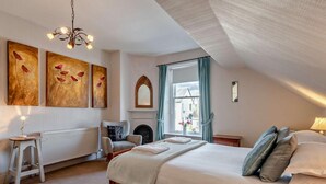 Een slaapkamer met een houten bed, een radiator, een stoel, een open haard en kunst aan de muur.