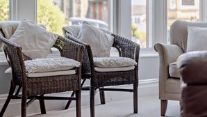 Wicker-stoelen met witte kussens en een beige fauteuil in een kamer met grote ramen.