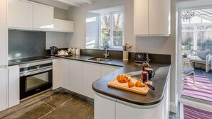 A modern kitchen with white cabinetry, a built-in oven, a large window, and a breakfast bar with croissants. - 2 Bed in Launceston (oc-84660) (Tregeare)