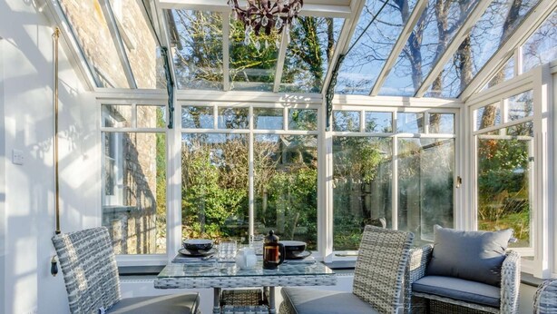 A sunlit room with wicker furniture, a glass ceiling, and a view of greenery outside. - 2 Bed in Launceston (oc-84660) (Tregeare)