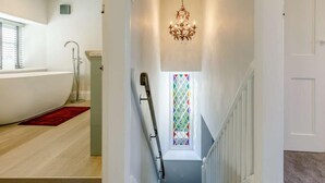 A hallway with a staircase, a chandelier, a window with stained glass, and a bathtub in the background. - 2 Bed in Launceston (oc-84660) (Tregeare)