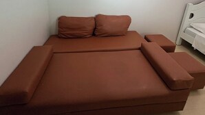 Quarto individual com uma cama de molas marrom, mesa de cabeceira e cabeceira branca.