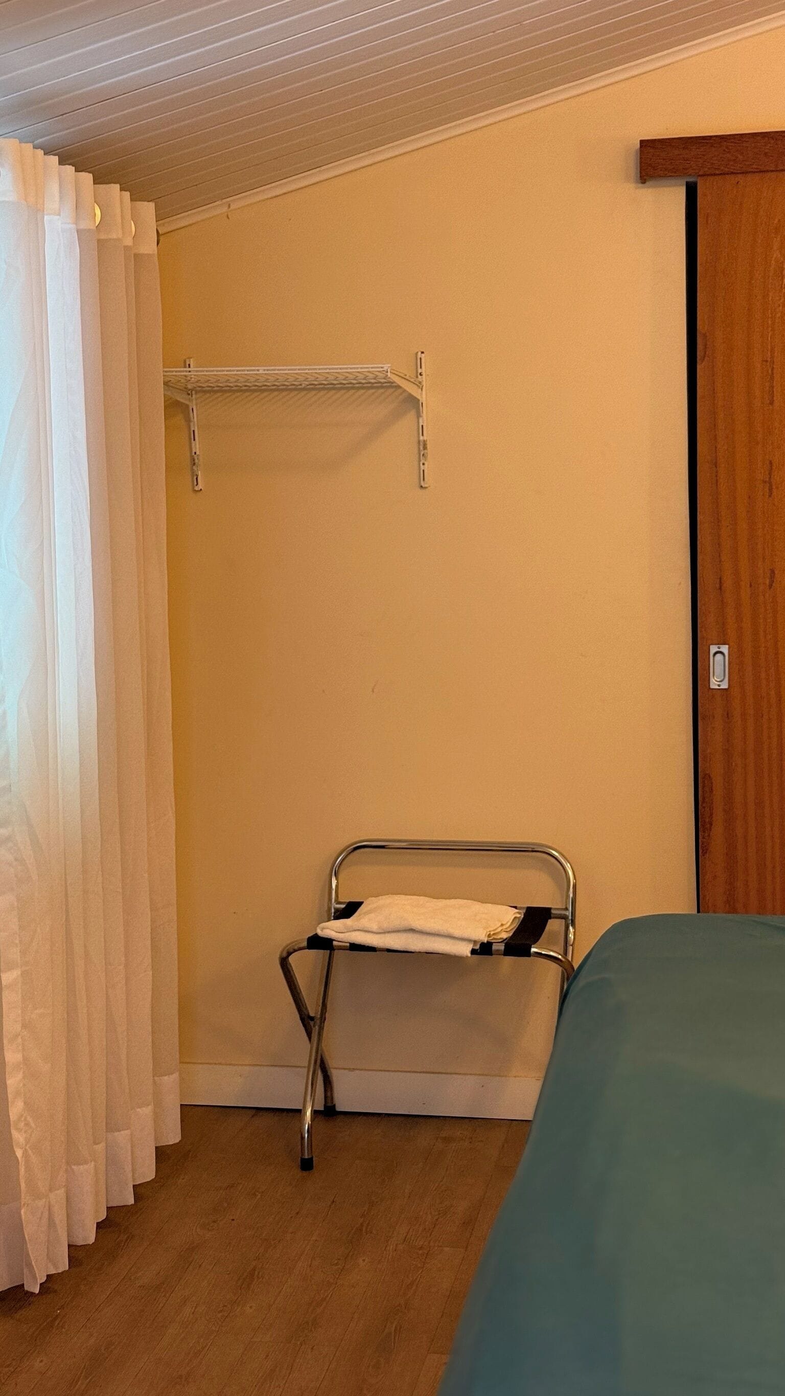 A room with a metal bed frame, a wooden door, and a metal shelf against the wall.