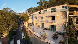 Un edificio de varios pisos con balcones, mesas al aire libre y vista a la calle.
