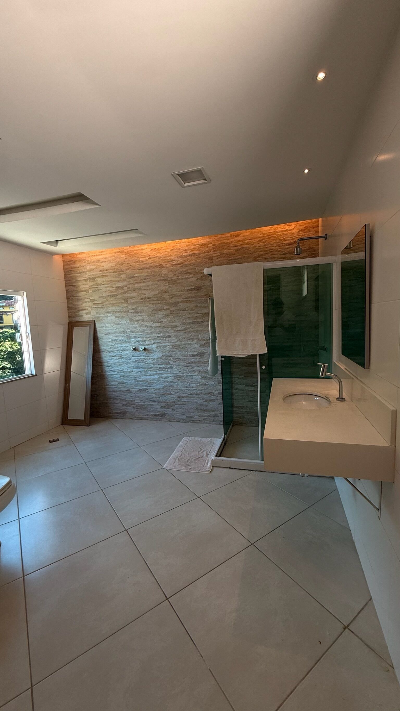 Uma casa de banho moderna com um espelho grande, uma pia e zona de duche.