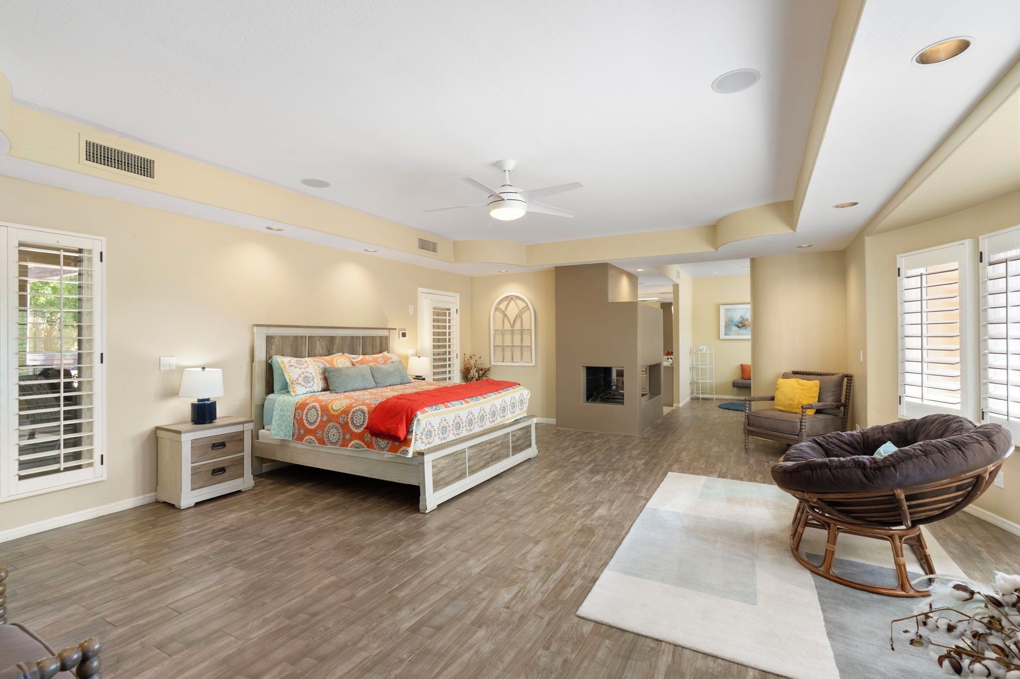 A spacious bedroom with a large bed, a ceiling fan, and a view of the living area.
