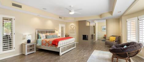 A spacious bedroom with a large bed, a ceiling fan, and a view of the living area.