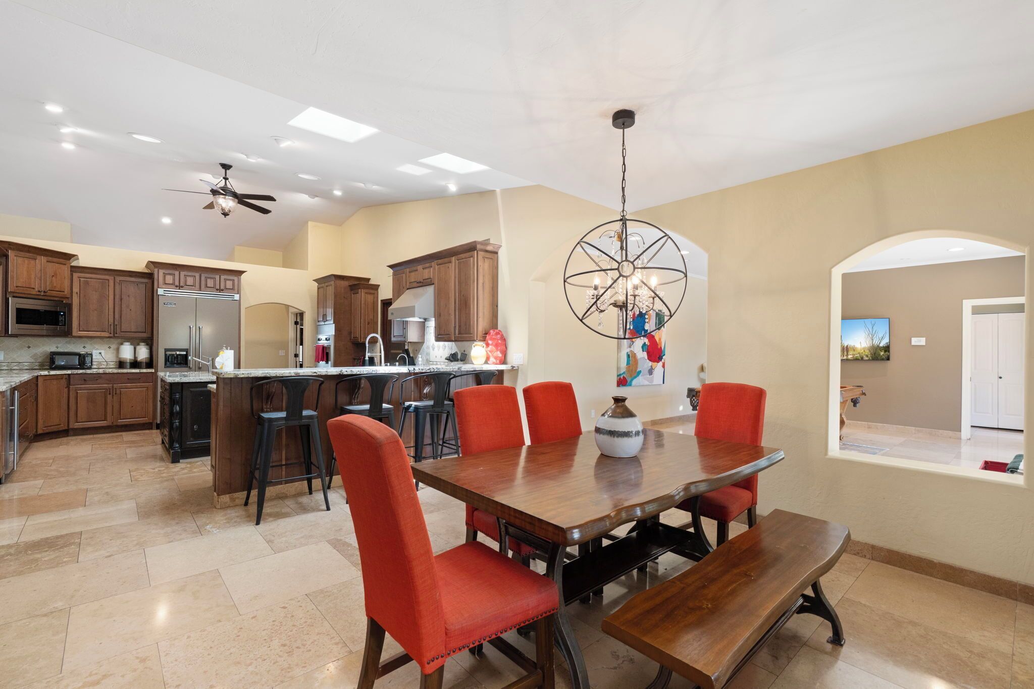 A spacious kitchen with wooden cabinets, a central island, and a dining area with a wooden table and red chairs.