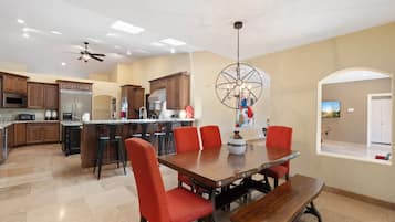 A spacious kitchen with wooden cabinets, a central island, and a dining area with a wooden table and red chairs.