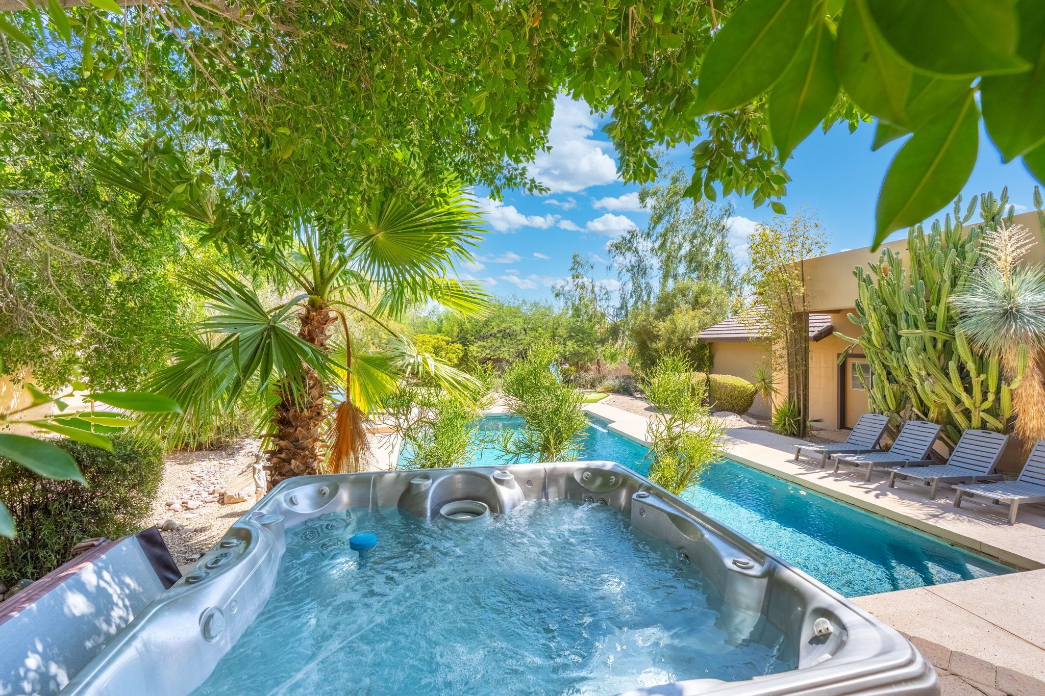 A hot tub surrounded by lush greenery and a poolside area with lounge chairs.