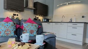 Una cocina moderna con horno empotrado, microondas y fregadero. Hay un comedor con sofá y mesa de centro.