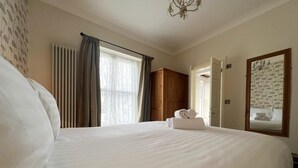 Habitación de hotel con una cama grande, un armario de madera, un espejo y una ventana con cortinas.