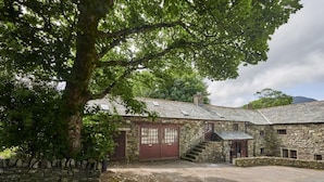 Un bâtiment en pierre avec un grand arbre devant, une porte rouge et un escalier menant à un étage supérieur.