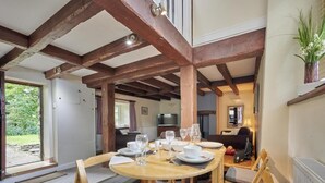Un coin repas avec une table et des chaises en bois, une vue sur l’extérieur et une cuisine en arrière-plan.