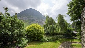 Un jardin avec un sentier de pierres, une végétation luxuriante et une montagne en arrière-plan.