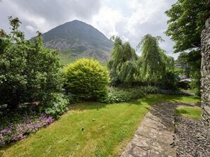 Un jardín con un sendero de piedra, abundante vegetación y una montaña al fondo.