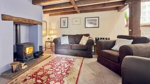 Un salon chaleureux avec une cheminée, deux canapés, un tapis à motifs et des poutres en bois au plafond.