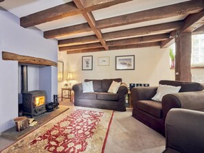 Una sala de estar acogedora con chimenea, dos sofás, un tapete estampado y vigas de madera en el techo.
