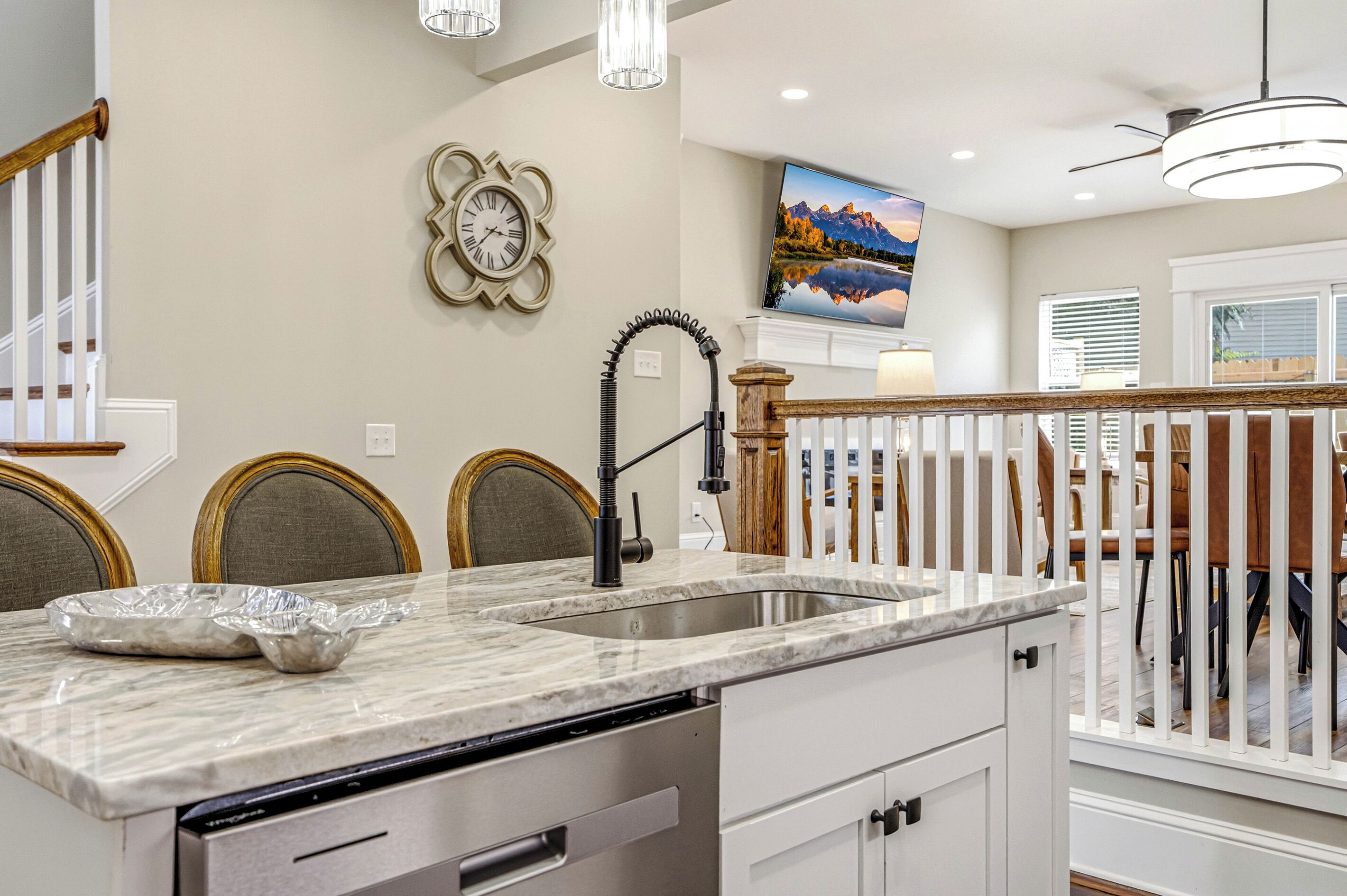 A kitchen with a marble countertop, a sink, a clock, and a dining area with chairs.