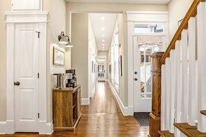 A hallway with a wooden floor, white doors, and a staircase with wooden railings. - The Clifton | Bars, Bourbon, and Brunch on Foot | Sleeps 15 (Louisville)