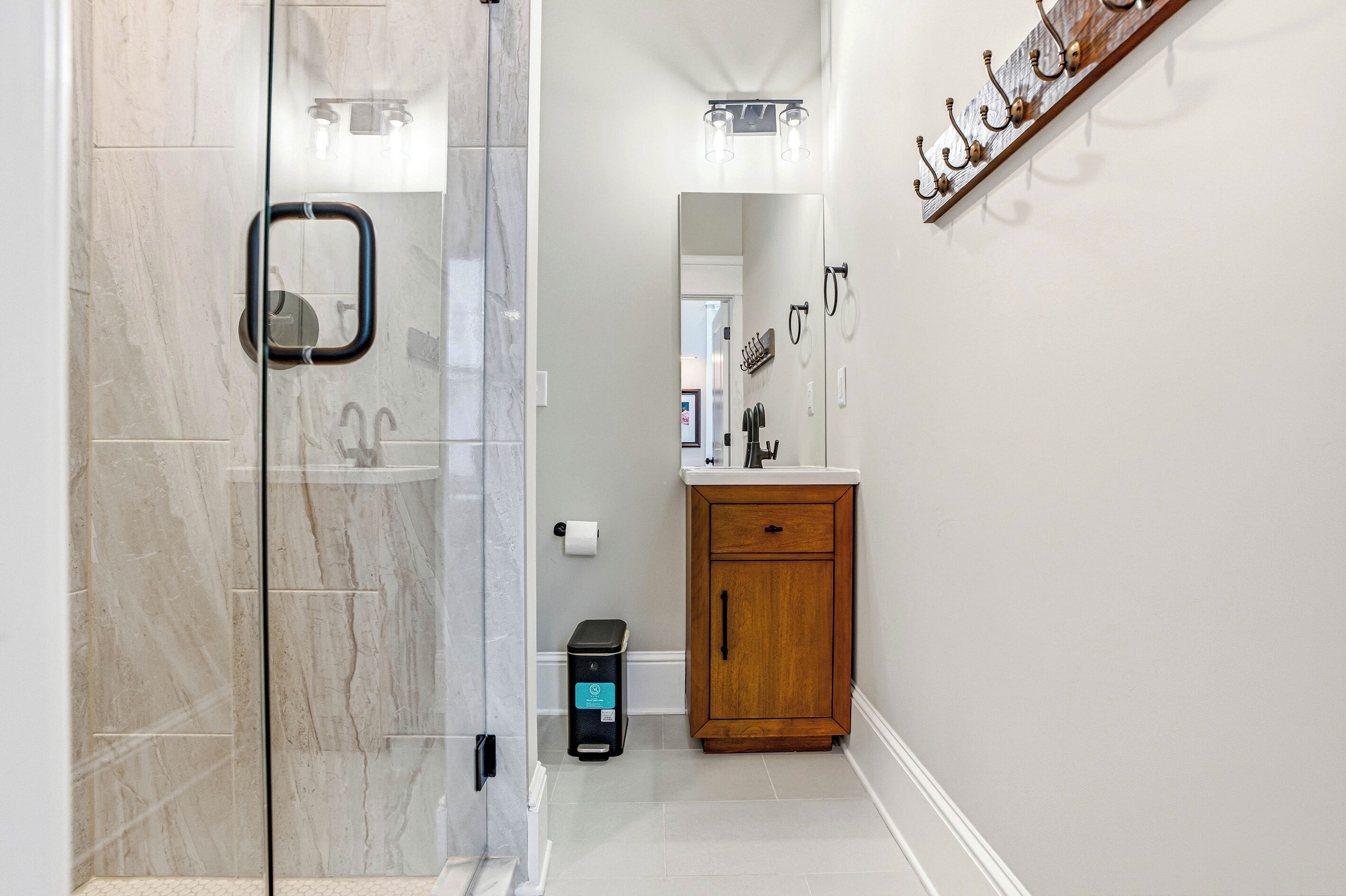 A bathroom with a glass shower door, a wooden cabinet, and a mirror.