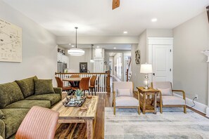 A living room with a sectional sofa, a wooden coffee table, and a dining area with a table and chairs. - The Clifton | Bars, Bourbon, and Brunch on Foot | Sleeps 15 (Louisville)