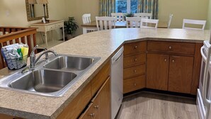 Een keuken met een dubbele spoelbak, houten kastjes, een vaatwasser, en een eethoek met een tafel en stoelen.