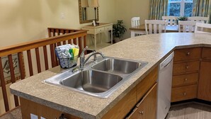 Een keuken met een granieten aanrecht, een roestvrijstalen spoelbak, houten kastjes, een vaatwasser en een brandblusser.