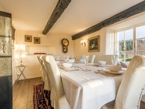 Une salle à manger avec une table dressée pour quatre personnes, une horloge au mur et une fenêtre donnant sur des arbres.