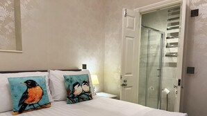 Une chambre d’hôtel avec un lit, deux oreillers ornés de motifs d’oiseaux, une porte de douche en verre et une pile de serviettes blanches.