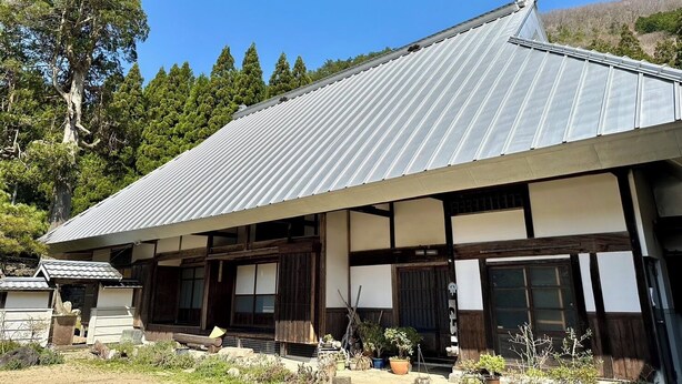 Il s’agit d’un bâtiment traditionnel japonais, doté d’un toit métallique à pente, de poutres en bois et d’un porche à l’avant, agrémenté de plantes en pot.