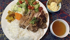Une assiette avec de la viande grillée, du riz, une salade et une tasse de thé.