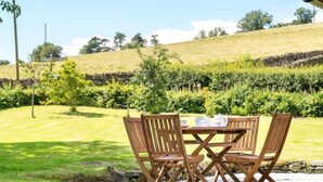 A wooden table and chairs set outdoors with a grassy area and a stone wall in the background. - 2 Bed in Penrith (oc-sz271) (Bampton)