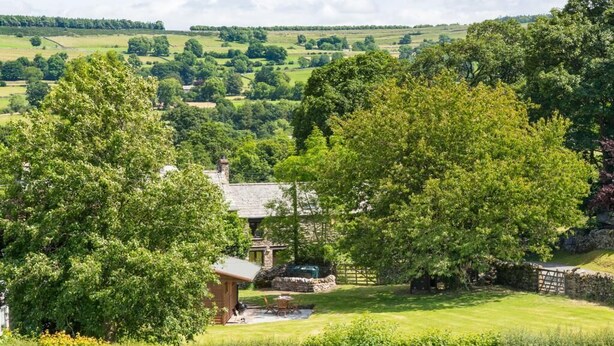 A rural house with a stone chimney, surrounded by lush greenery and a well-maintained lawn. - 2 Bed in Penrith (oc-sz271) (Bampton)