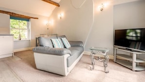 Ein modernes Wohnzimmer mit Sofa, Glastisch und Flachbildfernseher.