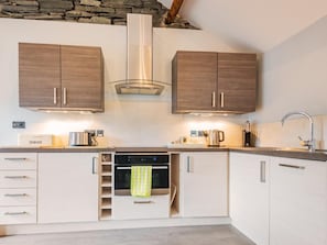 A modern kitchen with two wooden cabinets, a built-in oven, and a stone wall. - 1 Bed in Keswick (oc-sz177) (Keswick)