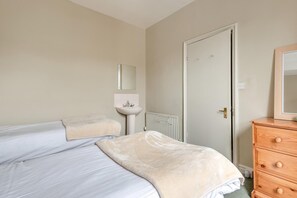 Ein Schlafzimmer mit zwei Betten, einem Nachttisch, einer Kommode, einem Spiegel und einem Heizkörper.