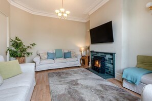Ein Wohnzimmer mit einer Couch, einem Kamin, einem Fernseher und einer Pflanze.