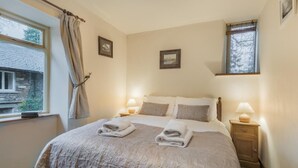 Ein Schlafzimmer mit einem Bett, zwei Nachttischlampen, einem Fenster mit Vorhängen und einem kleinen Bild an der Wand.