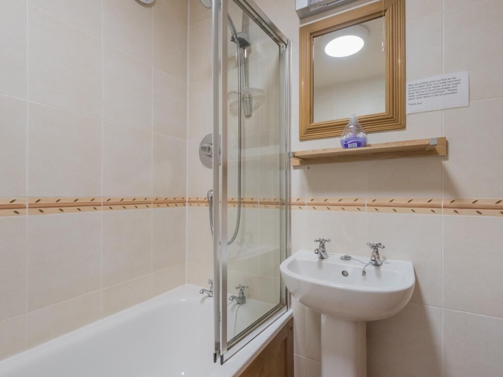 A bathroom with a glass-enclosed shower, a white sink, and a mirror above it.