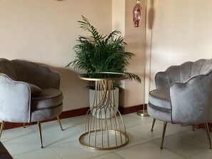 A room with two grey upholstered armchairs, a round table with a gold base, and a potted plant. - B&B verdi (Lecce)
