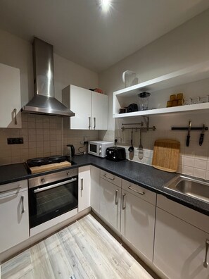 Eine moderne Küche mit weißen Schränken, einer Edelstahl-Dunstabzugshaube, einer Mikrowelle, einem Toaster und einem Holzer Schneidebrett.