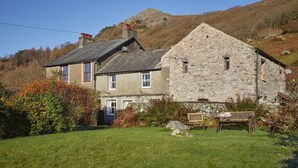 A stone building with a sloped roof, a wooden bench, and a grassy yard. - 3 Bed in Holmrook (oc-sz313) (Boot)