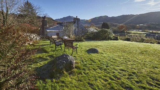 A grassy outdoor area with a stone wall, a bench, and a table. - 3 Bed in Holmrook (oc-sz313) (Boot)