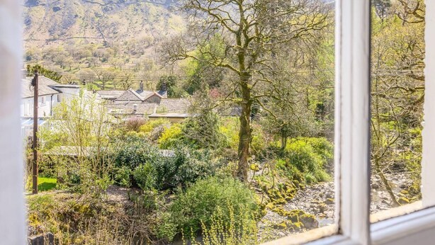 A window view of a rural landscape with mountains, a tree, and a building with a sloped roof. - 3 Bed in Keswick (oc-sz234) (Borrowdale)