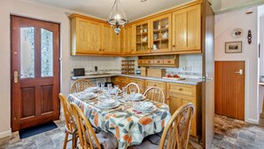 Una cocina con armarios de madera, una mesa de comedor para cuatro comensales y una araña.