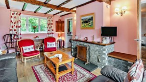 Una sala de estar acogedora con vigas de madera a la vista, chimenea, televisor y asientos cómodos.