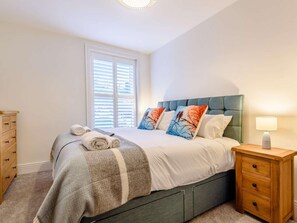 Een slaapkamer met een bed, nachtkastje, kast en een raam met jaloezieën.